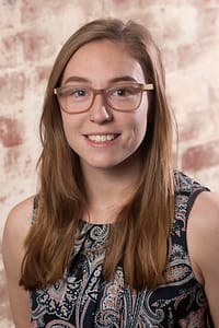 alt="Portrait of Jade Conlon, smiling against an exposed brick background"