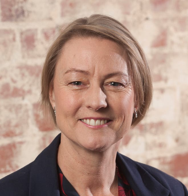 alt="Portrait of Karen Conlon, smiling against a exposed brick background"