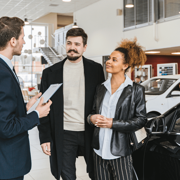 alt="three people engaged in discussion in a car dealership"